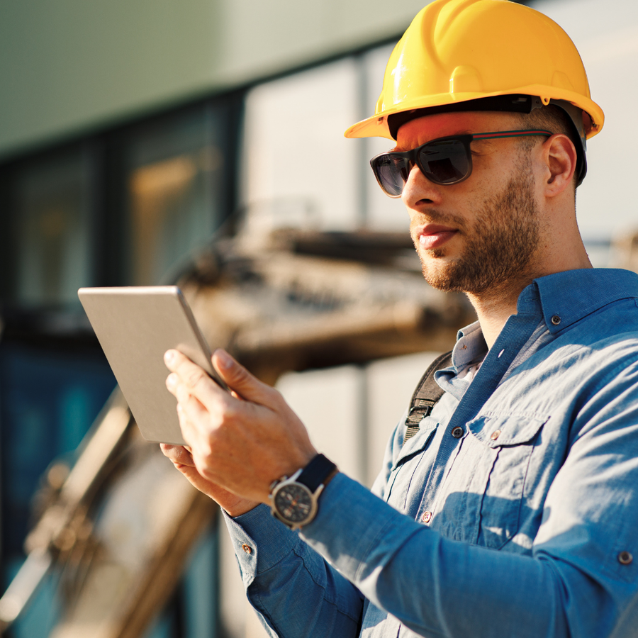 Man in construction attire using a tablet outdoors