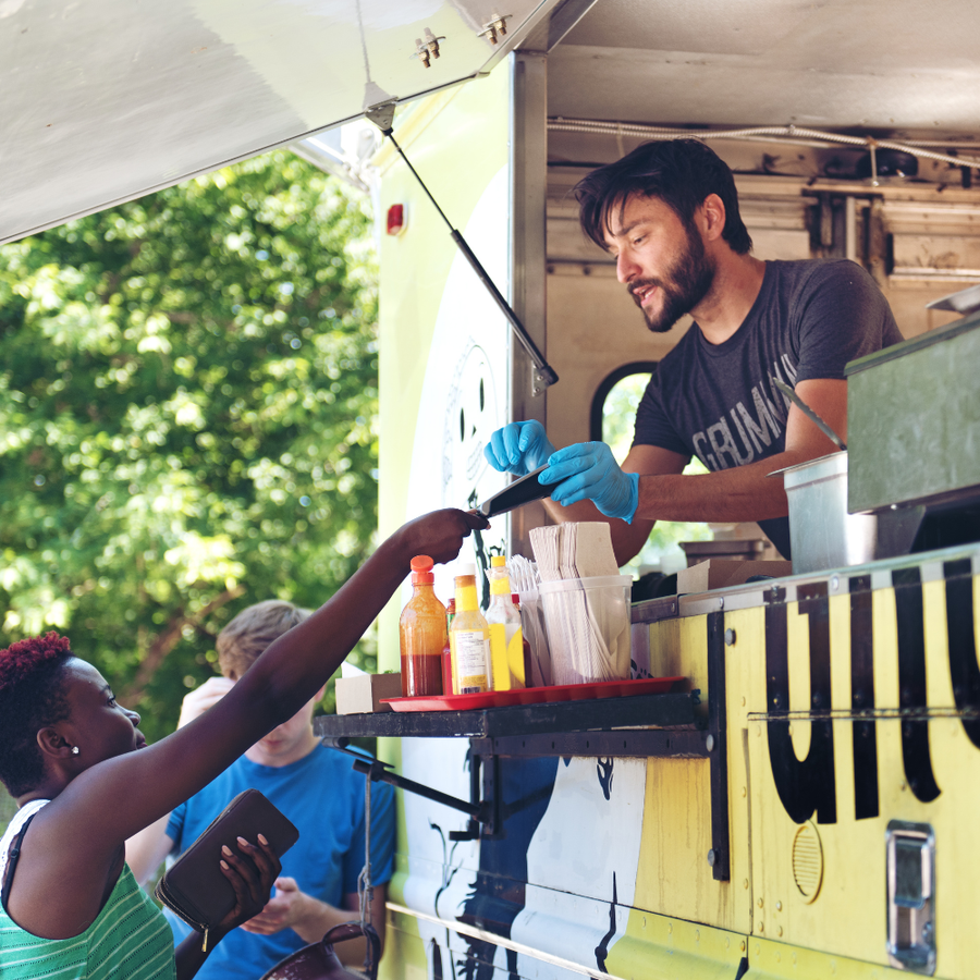 Person receiving food from a food truck vendor with a customer.