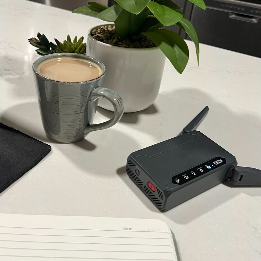 Black m106 pro router on a desk with a mug of coffee and plants in the background